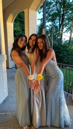 three beautiful young women standing next to each other in front of a building holding hands