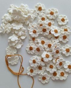 crocheted white and orange flowers are laying on the ground next to an orange string