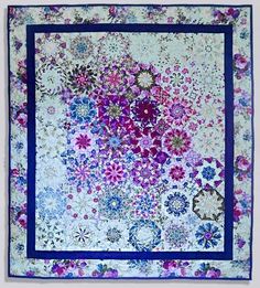 a quilted wall hanging with purple and blue flowers on the bottom, in front of a white background