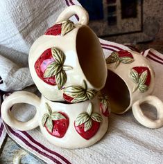 three ceramic strawberry teapots sitting on top of a towel