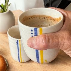 a man holding two cups of coffee on top of a wooden table