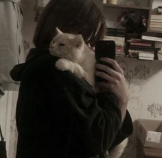 a woman holding a cat in her arms while taking a selfie with her cell phone