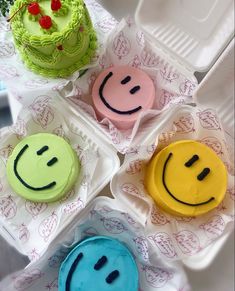 four decorated cakes in plastic containers with faces on the top and one has a green frosting