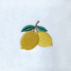 two yellow lemons with green leaves embroidered on white fabric, sitting next to each other