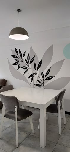 a white table sitting under a lamp next to a wall with leaves painted on it