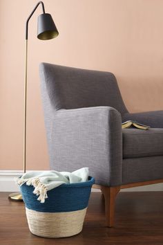 a chair with a blanket on it next to a floor lamp and a blue basket