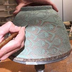 a person working on a lamp shade with a wooden stick in front of it and another hand holding a piece of wood