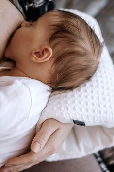 a woman holding a baby in her arms while laying on top of a bed next to a pillow