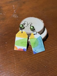 two earrings are sitting on top of a piece of wood and one has a tag attached to it