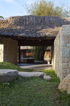 an outdoor area with grass, rocks and a thatch roofed hut in the background