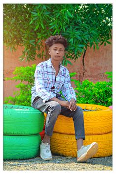 a young man sitting on top of a pile of green and yellow tire rims