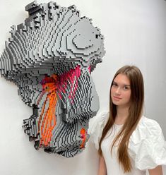 a woman standing in front of a wall sculpture made out of legos with an orange and red design on it