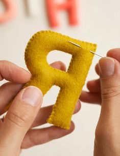 a person is holding a needle and sewing the letter p into a piece of felt