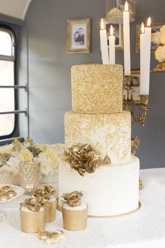 there is a wedding cake with gold decorations on the table and candles in the background