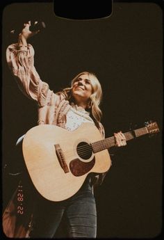 a woman holding a guitar and singing into a microphone