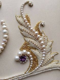 two pieces of jewelry with pearls and other beads on white fabric, one piece has a purple stone in the center