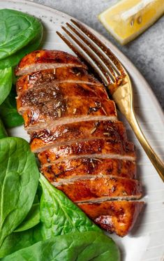 a white plate topped with meat next to spinach leaves and a gold fork on top of it