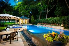 an outdoor dining area next to a swimming pool at night with patio furniture and umbrellas