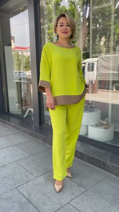 a woman is standing on the sidewalk wearing bright yellow pants and a green top with grey trim