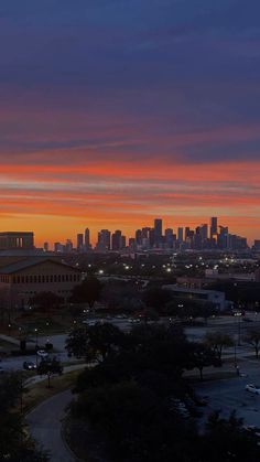 the sun is setting over a city with skyscrapers in the distance and cars parked on the street