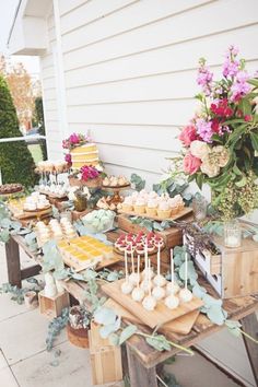 a table filled with cakes and cupcakes on top of wooden trays next to flowers