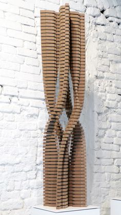 a sculpture made out of strips of cardboard sitting on top of a white brick wall