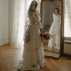 a woman standing in front of a mirror wearing a wedding dress and holding a bouquet