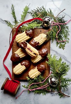 chocolates and candy on a wooden board with christmas decorations around the edges, along with twine of red ribbon