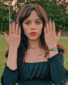 a woman with her hands on her face and two fingers up to her head, in front of a soccer field