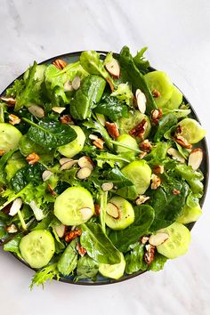 a salad with spinach and almonds in a black bowl on a marble table