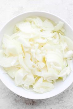 a white bowl filled with chopped onions on top of a marble countertop next to a knife