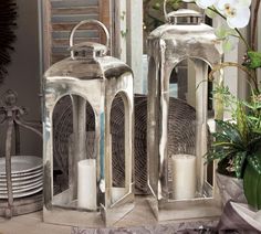 two silver lanterns sitting on top of a table next to plates and flowers in front of a mirror