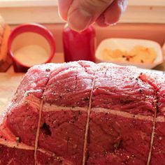 a hand is sprinkling seasoning on a large piece of meat