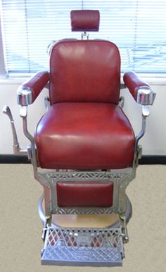 a red chair sitting in front of a window next to a metal shelf with scissors on it