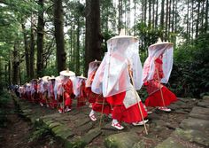 a group of people dressed in red and white outfits walking through the woods with umbrellas on their heads