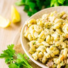 a bowl filled with macaroni salad next to some parsley on the table