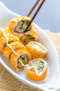 sushi rolls with chopsticks in a white dish on a bamboo mat, ready to be eaten