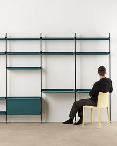 a man sitting on a chair in front of a bookshelf with shelves behind him