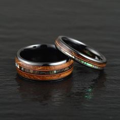 two wedding bands with green and brown wood inlays are shown on a black surface