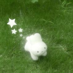 a small white teddy bear sitting in the grass with stars coming out of it's back