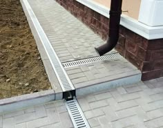 a pipe is attached to the ground in front of a brick building with a drain