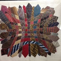 a quilted wall hanging with many different colored ties on it's sides and an intricate design in the middle