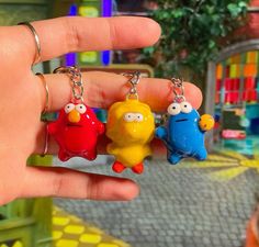 three different colored key chains in the shape of cartoon characters are being held by someone's hand