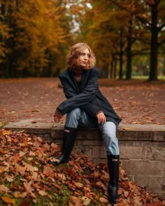 a woman sitting on top of a stone bench surrounded by leaves