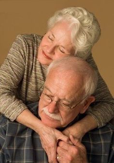 an elderly man hugging his wife on the cheek