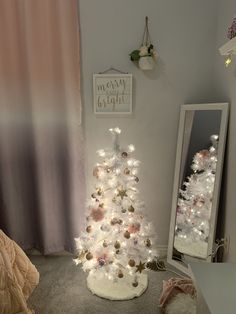 a white christmas tree in a bedroom next to a mirror with lights and decorations on it