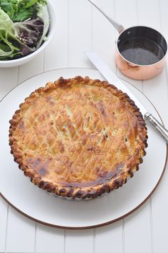 a pie on a plate next to a bowl of salad