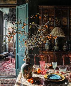 a dining room table with oranges and vases on it, in front of a blue door