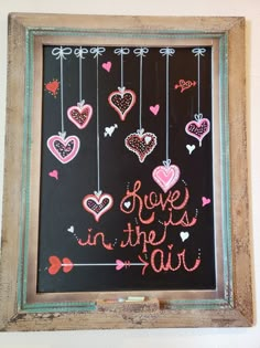 a chalkboard with hearts hanging from it and the words love is in the air