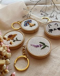 four embroidered keychains with cats and flowers on them sitting on a white cloth